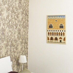 May include: A white bed with a burgundy bedspread and two striped pillows. A white lamp sits on a bedside table next to the bed. A framed print of a building with arches hangs on the wall behind the bed.