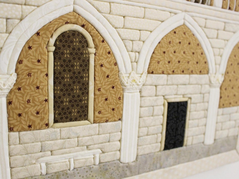May include: A close-up of a white brick wall with two arched doorways and a window. The doorways have a brown and gold patterned fabric behind them. The window has a black and brown patterned glass.