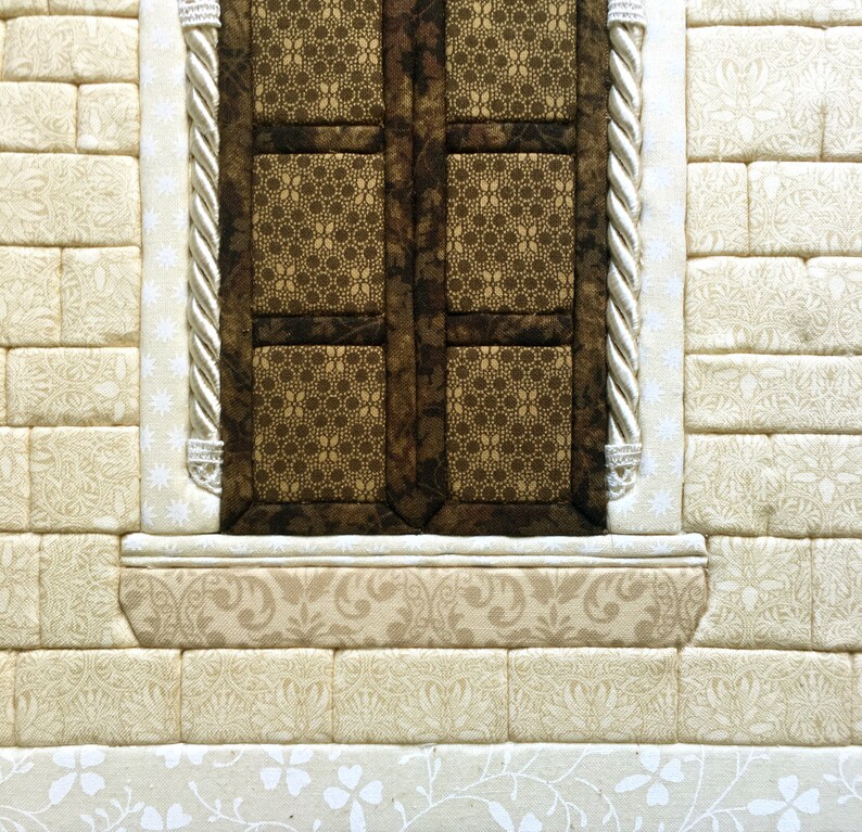 May include: A close-up of a brown window with a white frame and a decorative trim. The window is set into a wall made of beige fabric squares.