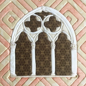 May include: A white fabric applique of a gothic arch window with three arched sections and a brown fabric background with a repeating pattern.