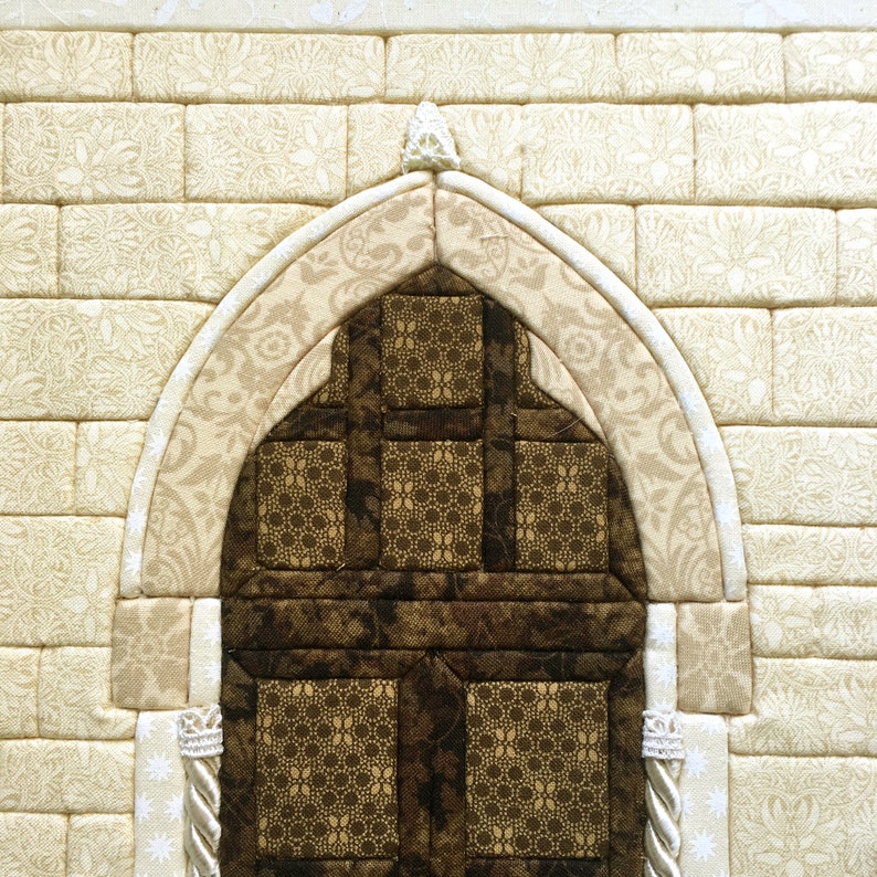 May include: A beige fabric wall with a brown fabric arched doorway. The doorway is made of squares and has a decorative pattern.