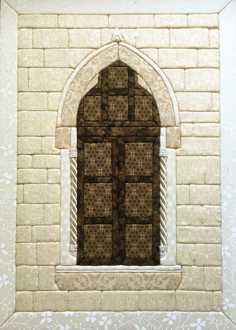 May include: A quilted wall hanging featuring a brown arched window with a decorative design. The window is set against a white brick wall with a floral pattern.