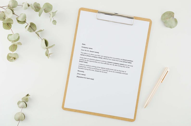 May include: A clipboard with a white sheet of paper and a silver clip, with a resignation letter printed on it. A gold pen rests beside the clipboard. Eucalyptus leaves and a small green leaf are arranged around the clipboard on a white surface.