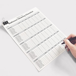 May include: A bathroom cleaning checklist with a black binder clip. The checklist is being filled out with a red and black pen. The checklist includes sections for morning, afternoon, evening, night, and closing.