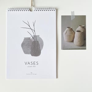 May include: A white spiral-bound calendar featuring a minimalist illustration of vases and branches. The text "VASES calendar 2026" is printed below the illustration. A small photograph of three vases is taped to the right.