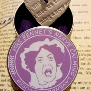 Könnte beinhalten: Eine runde, violette Dose mit einem weißen Bild einer Frau mit einem überraschten Ausdruck. Die Dose trägt den Text "Mrs. Bennet's Nerve Calming Lavender Diffuser" am Rand.