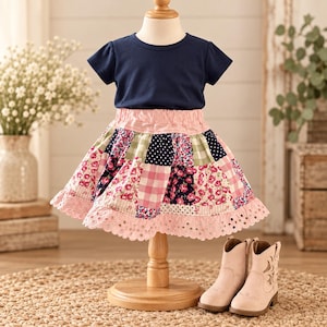 Könnte beinhalten: Ein marineblaues T-Shirt mit kurzen Ärmeln und ein Patchwork-Rock mit rosa, weißen und marineblauen Blumen-, Punkte- und Vichy-Karomustern. Der Rock hat einen rosa Gummibund und einen Saum aus Lochstickerei, dazu ein Paar hellbraune Stiefel.