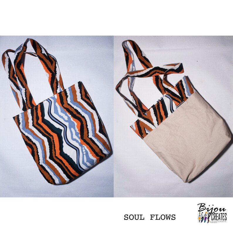Pode incluir: Uma bolsa tote revers&iacute;vel com um padr&atilde;o ondulado preto, laranja e azul de um lado e uma tela bege lisa do outro. A bolsa tem duas al&ccedil;as longas. O texto "SOUL FLOWS" est&aacute; impresso abaixo da bolsa.