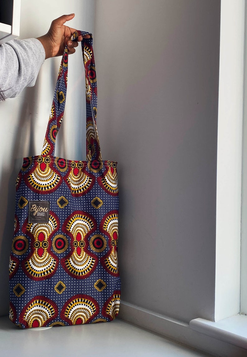 Pode incluir: Uma bolsa tote azul e vermelha com um padr&atilde;o geom&eacute;trico. A bolsa tem uma etiqueta branca com o texto "Bijou Crafted" nela.
