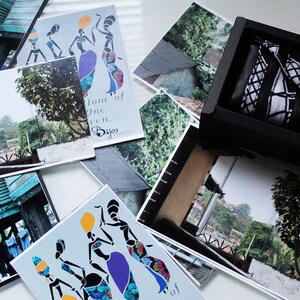 May include: A set of postcards featuring colourful illustrations of women in traditional African clothing. The postcards have a white background and feature the text "From one woman... Byjo Designs".