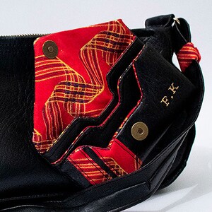 May include: Black leather bag with a red and gold patterned flap. The bag has a gold metal button and the initials "F.K." are embossed on the front.