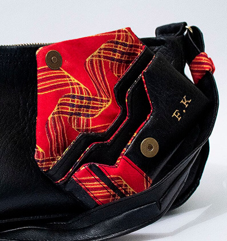 May include: Black leather bag with a red and gold patterned flap. The bag has a gold metal button and the initials "F.K." are embossed on the front.