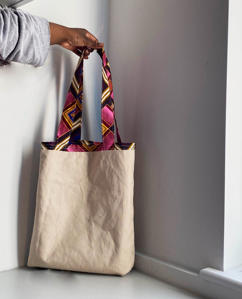 Pode incluir: Uma bolsa tote de lona bege com al&ccedil;as de tecido estampado em rosa, amarelo, azul e preto.