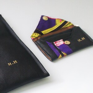 May include: Two black leather wallets with gold lettering. The smaller wallet is open, revealing a colourful patterned fabric lining. Both wallets have the initials "H.H." embossed on the front.