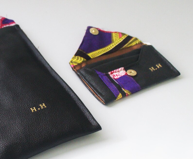 May include: Two black leather wallets with gold lettering. The smaller wallet is open, revealing a colourful patterned fabric lining. Both wallets have the initials "H.H." embossed on the front.
