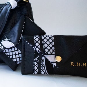 May include: A black leather wallet with a white and black patterned flap. The wallet has a gold button and the initials "R.H.H." are embossed on the front.