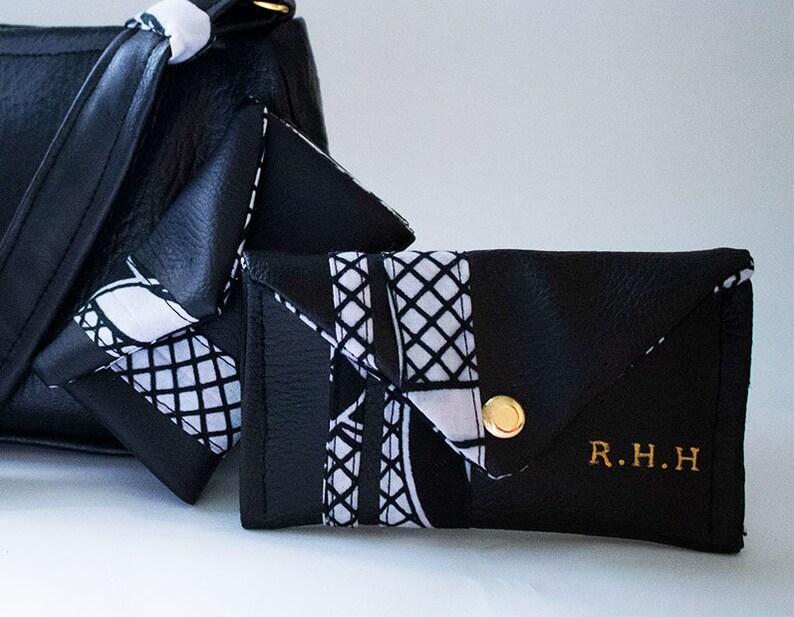 May include: A black leather wallet with a white and black patterned flap. The wallet has a gold button and the initials "R.H.H." are embossed on the front.