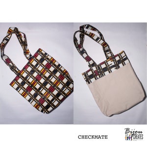 Pode incluir: Uma bolsa de tecido reutiliz&aacute;vel com um padr&atilde;o xadrez preto, branco, vermelho e amarelo em um lado e uma tela bege lisa no outro. A bolsa tem duas al&ccedil;as de tecido. O texto "CHECKMATE" est&aacute; impresso abaixo da bolsa.