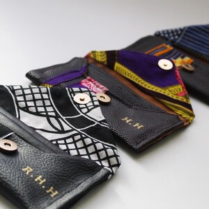 May include: Four black leather wallets with different patterned fabric accents. Each wallet has a gold button closure and the initials "R.H.H" embossed on the front.