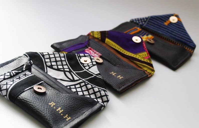 May include: Four black leather wallets with different patterned fabric accents. Each wallet has a gold button closure and the initials "R.H.H" embossed on the front.