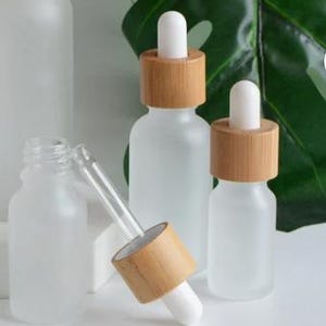 May include: Frosted glass dropper bottles with bamboo lids and white droppers. The bottles are in various sizes, with one bottle open and the dropper separate. The bamboo lids add a natural touch to the bottles.