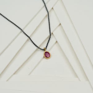 May include: A delicate gold chain necklace with a small, oval-shaped pink gemstone pendant.