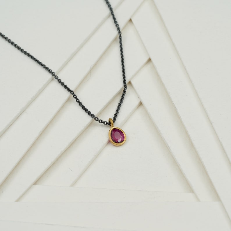 May include: A delicate gold chain necklace with a small, oval-shaped pink gemstone pendant.
