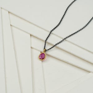 May include: A delicate gold and black chain necklace with a small pink gemstone pendant.