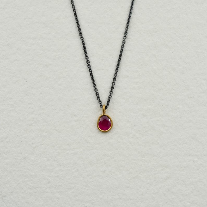 May include: A delicate silver chain necklace with a small, round, red gemstone pendant.