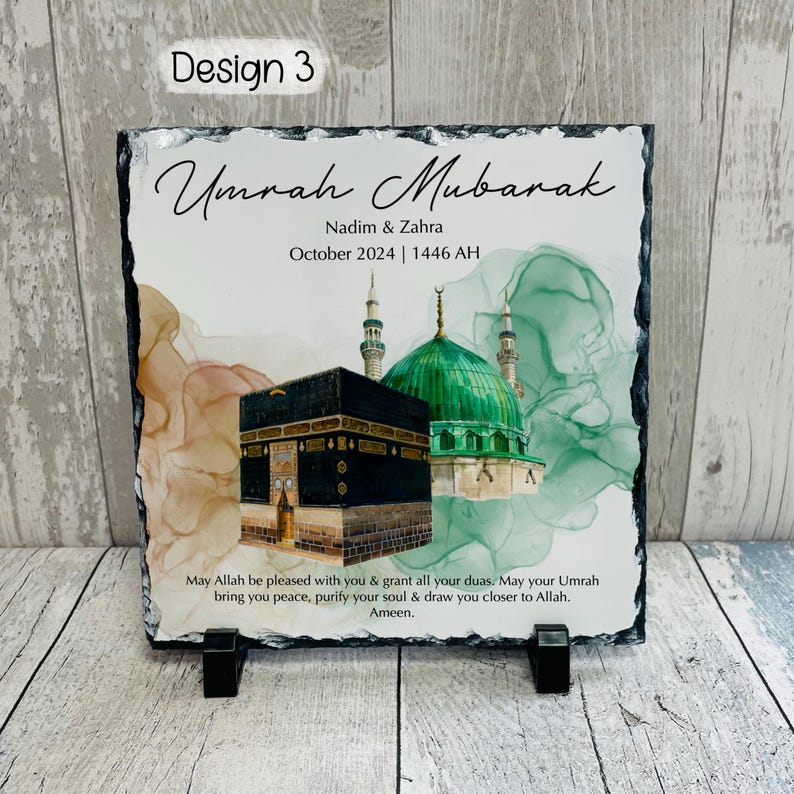 Pu&ograve; includere: Una targa in ardesia nera con un'immagine ad acquerello della Kaaba e una cupola verde. Il testo "Umrah Mubarak" &egrave; scritto in un carattere decorativo, insieme ai nomi "Nadim & Zahra" e la data "Ottobre 2024 | 1446 AH". La targa include anche un messaggio che augura pace, purificazione e vicinanza ad Allah.