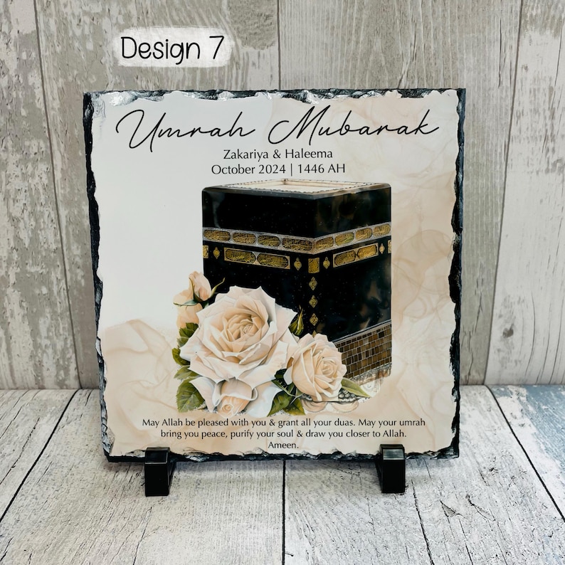 May include: A white slate plaque with a black and gold image of the Kaaba, a white floral design, and the text "Umrah Mubarak Zakariya & Haleema October 2024 | 1446 AH" and "May Allah be pleased with you & grant all your duas. May your umrah bring you peace, purify your soul & draw you closer to Allah. Ameen."