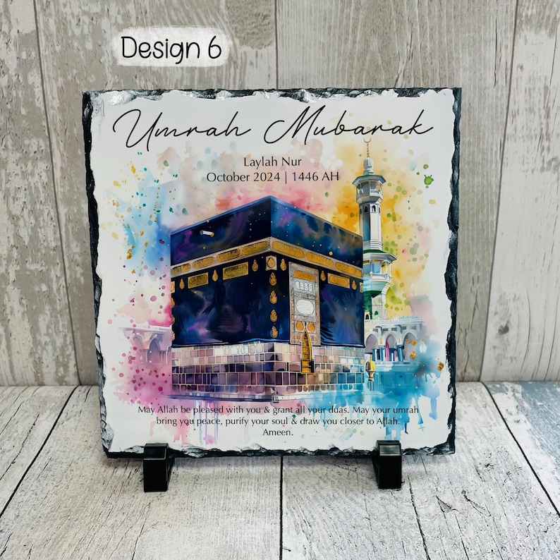 May include: A black slate plaque with a watercolor painting of the Kaaba in Mecca. The plaque has the text "Umrah Mubarak" and "Laylah Nur October 2024 | 1446 AH" and a message wishing the person a blessed Umrah.