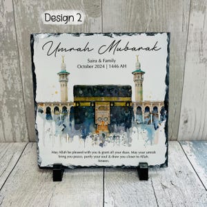 Pu&ograve; includere: Una targa in ardesia nera con un'illustrazione ad acquerello della Kaaba a La Mecca, in Arabia Saudita. Il testo "Umrah Mubarak" &egrave; scritto in un carattere decorativo nella parte superiore della targa. Il testo "Saira & Family October 2024 | 1446 AH" &egrave; scritto sotto l'illustrazione. La targa include anche un messaggio di benedizioni e una preghiera per la pace e la purificazione.