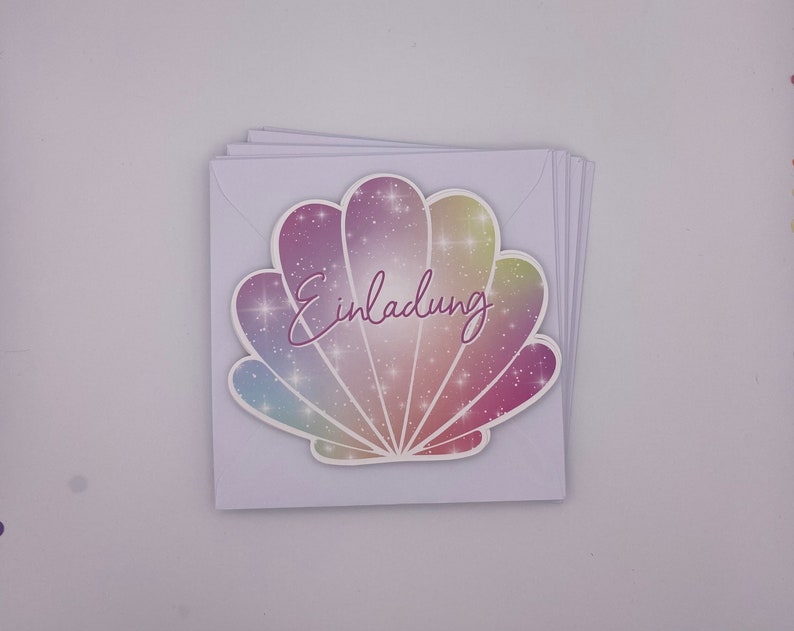Pu&ograve; includere: Un biglietto bianco con un design a conchiglia iridescente scintillante. Il testo "Einladung" &egrave; scritto in corsivo rosa sulla conchiglia.