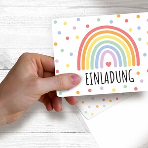May include: A white card with a rainbow and colorful polka dots. The card says "EINLADUNG" which is German for "Invitation".