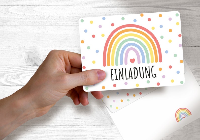 May include: A white card with a rainbow and colorful polka dots. The card says "EINLADUNG" which is German for "Invitation".