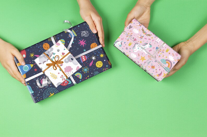 May include: Two wrapped gifts on a green background. One is wrapped in dark blue paper with a space-themed pattern, and a smaller gift on top with a koala pattern. The other gift is wrapped in pink paper with a unicorn and rainbow pattern.