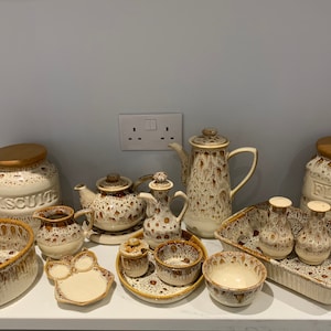 May include: A collection of 14 vintage ceramic kitchenware items in a brown and white speckled pattern. The items include a teapot, creamer, sugar bowl, salt and pepper shakers, a casserole dish, two canisters labeled "Biscuit" and "Flour", and a variety of bowls.