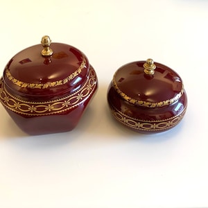 Może przedstawiać: Dwa ozdobne drewniane pudełka z pozłacanymi obramowaniami i pokrywkami. Większe pudełko jest ośmiokątne, a mniejsze okrągłe. Oba pudełka mają złoty guzik na pokrywce.