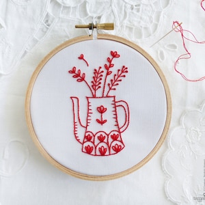 May include: Red embroidery hoop with a red embroidered design of a pitcher with flowers. The pitcher has a scalloped design and the flowers are simple stems with small red flowers.