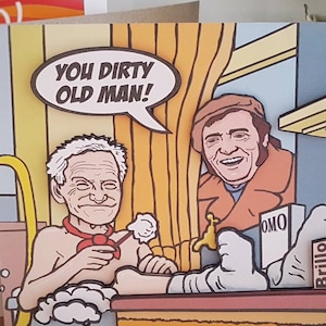 May include: A funny greeting card with a cartoon illustration. The card shows two men, one in a bathtub and the other standing. Text in a speech bubble says "YOU DIRTY OLD MAN!". Another card is visible in the background.
