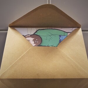May include: A brown paper envelope partially open, revealing a colorful illustration. The illustration depicts a person wearing a green shirt and blue pants. The envelope is made of a light brown paper material.
