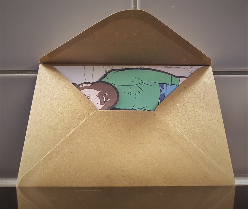 May include: A brown paper envelope partially open, revealing a colorful illustration. The illustration depicts a person wearing a green shirt and blue pants. The envelope is made of a light brown paper material.