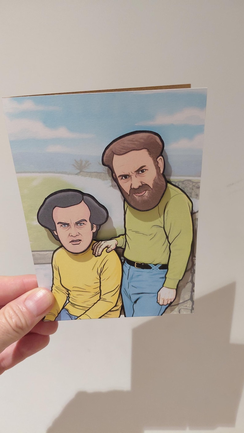 May include: Greeting card featuring a cartoon illustration of two men. One man has a beard and is wearing a yellow long-sleeve shirt and blue jeans. The other man is wearing a yellow long-sleeve shirt and blue jeans. The background shows a blue sky.