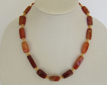 May include: A necklace made of carnelian beads with gold accents. The beads are rectangular and have a reddish-brown colour.