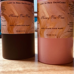 Op de afbeelding: Twee gezichtswasflessen van Lady in Red Skincure. Eén is donkerbruin, de andere roze. Beide hebben een etiket met de tekst "Honey Tea Tree Deep Clean Face Wash, Volume 59 ml."