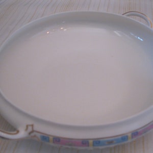 May include: White ceramic serving dish with two handles and a blue, pink, and gold trim around the edge.