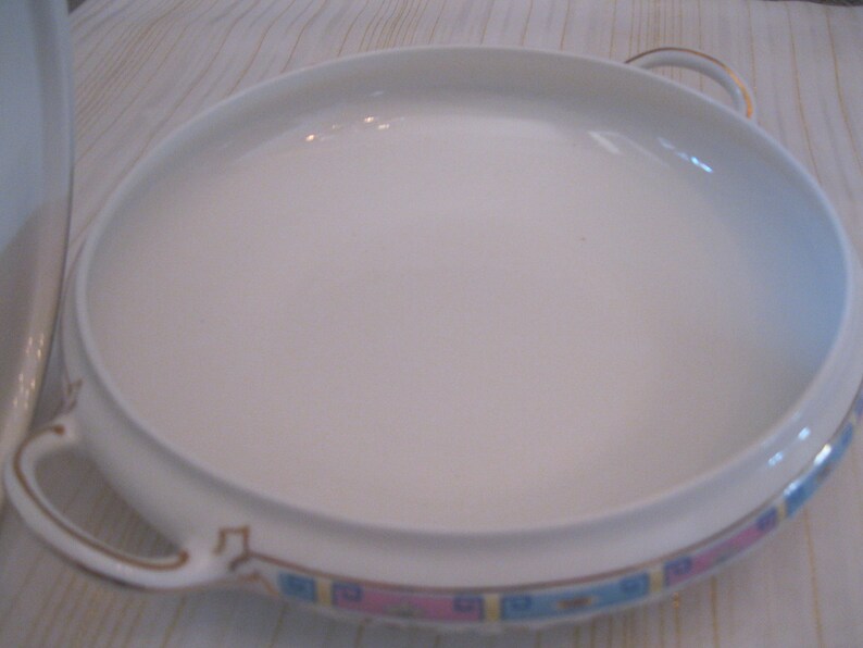 May include: White ceramic serving dish with two handles and a blue, pink, and gold trim around the edge.