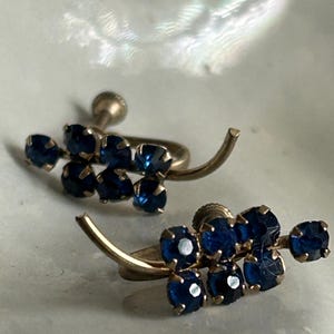 May include: A pair of vintage clip-on earrings with a cluster of blue rhinestones set in gold tone metal.