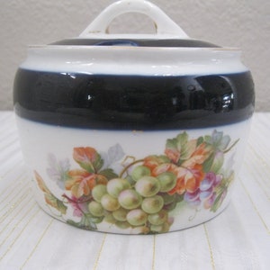 May include: White porcelain sugar bowl with a blue band and a floral design of grapes and leaves. The lid has a knob handle.